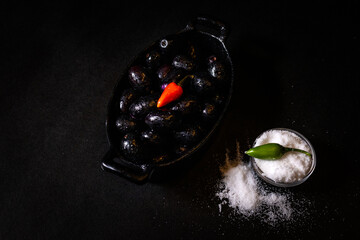 Indian blackberry or jamun with red and green chillies and a bowl of salt against dark background....