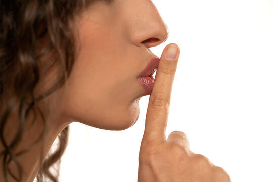 Cropped image of a young woman holding index finger at her lips, saying 'shh' on a white background. side profile view