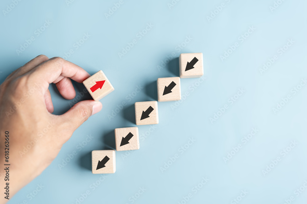 Leinwandbilder Hand holding wood block with Red arrow and different direction facing opposite direction with black arrow for business disruption and technology transformation and different thinking idea concept.
