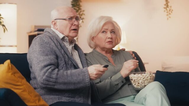 Anxious couple in their 60s overwhelmed by bad news, watching television at home