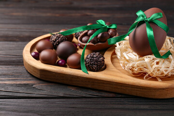 Tasty chocolate eggs with green bows and sweets on wooden table