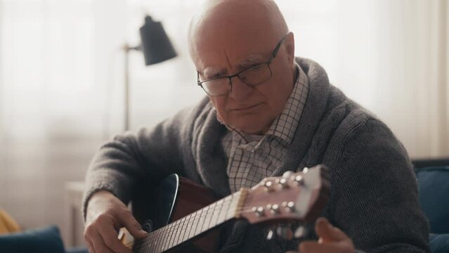 Pensive senior male practicing acoustic guitar play at home, musical hobby