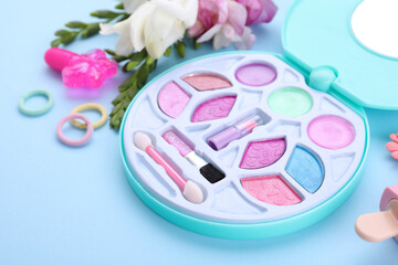 Decorative cosmetics for kids. Eye shadow palette, accessories and flowers on light blue background, closeup