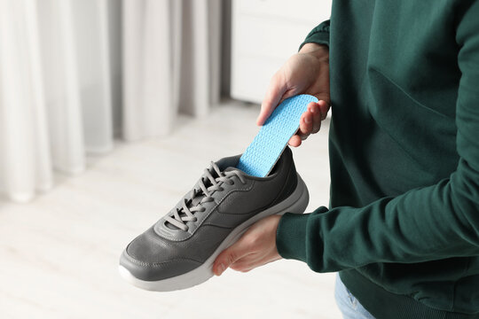 Man putting orthopedic insole into shoe indoors, closeup. Space for text