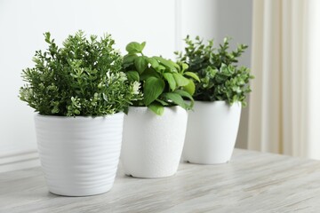 Different artificial potted herbs on white wooden table indoors, space for text