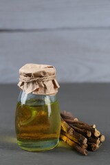 Dried sticks of licorice roots and essential oil on grey wooden table