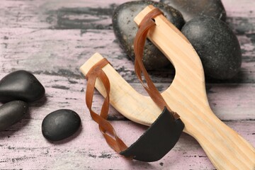 Slingshot with stones on old pink wooden background, closeup