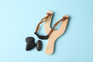 Wooden slingshot with stones on light blue background, flat lay