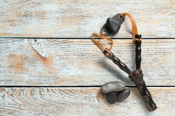 Black slingshot with stones on old light blue wooden table, flat lay. Space for text