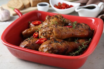 Chicken legs glazed in soy sauce with black sesame, chili pepper and thyme on light table, closeup