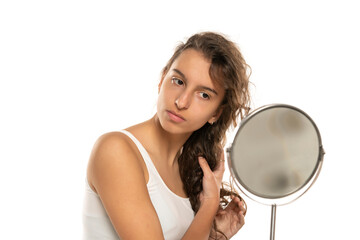 Young woman checking her long wavy hair in front of mirror on a white background