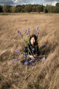 fine art portrait of asian girl sitting in a field holding purple flowers