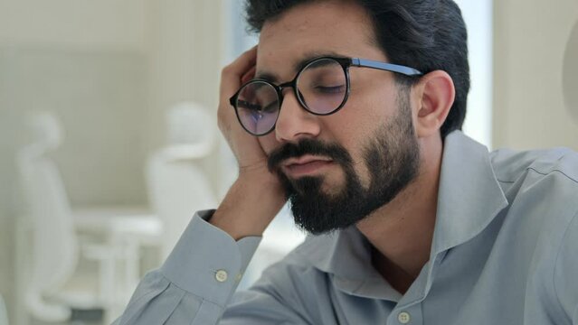 Lazy tired office worker Indian man guy sleepy fatigued bored businessman lean on hand sleep at workplace boring business work low energy burnout depression male drowsy weary exhausted entrepreneur
