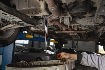 Auto mechanic drains old used engine oil at a service station, scheduled service maintenance of a...