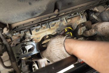 Auto mechanic installs a new manifold gasket for a passenger car engine, post-warranty service at a service station