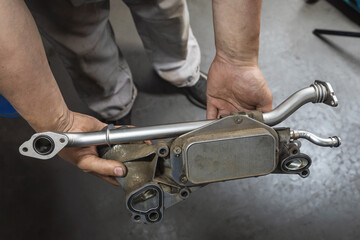 Obraz premium An auto mechanic holds in his hands a heat exchanger for a gasoline engine of a passenger car with cleaned tubes and new gaskets, post-warranty service in a car service