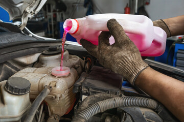 An auto mechanic at a service station pours antifreeze into the expansion tank of a car, a scheduled replacement of the engine coolant