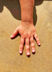 A hand in the sand on a bright, sunny day.