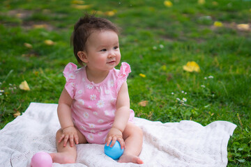 Fototapeta na wymiar happy and adorable 7 or 8 months old baby girl playing with ball toy cheerful sitting on towel lying on grass city park in childhood concept