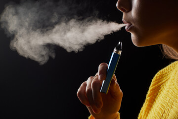 young girl smokes a vape close-up on a dark background