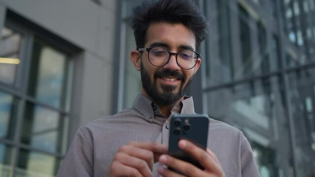 Happy excited winner Arabian Indian muslim businessman using smartphone outdoors winning job opportunity mobile phone win big prize amazed shocked man shout yes get business success victory in city