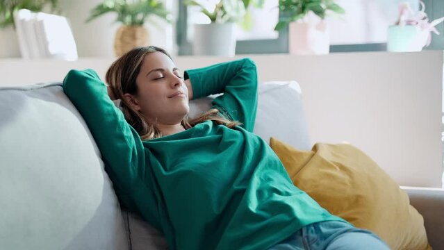 Video of young tired woman relaxing on couch with pillow for stomachache in living room at home.