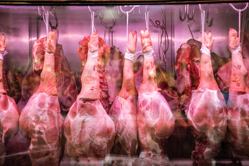 pig storage at butcher's stall. whole raw large pork leg hanging on hooks in refrigerator at meat...