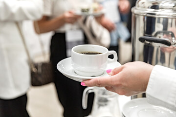 A woman's hand with a beautiful manicure holds a cup of coffee. Coffee break during the event. Catering for business events. Soft focus.