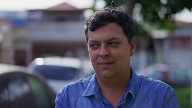 Thoughtful latin man with smirk in face, person having an idea, subtle eureka moment, close-up face standing outside in street