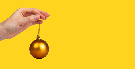 Gold brown Christmas ball, bauble, ornament on string, hanging in women hand. Yellow monochrome...