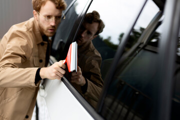 Attractive male worker washing his luxury car with window scraper. Concept of self-service