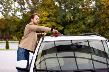 Portrait of bearded man wearing casual clothes and glasses wiping car roof with window squeegee