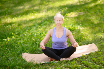 Athletic middle-aged woman doing yoga outdoors in a city park in a lotus position,closed eyes.Meditation,yoga,stretching