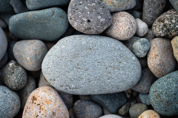 Fototapeta na wymiar Close-up, rounded pebble stone with space for text. Natural texture background. Sea beach stones around. Top view.