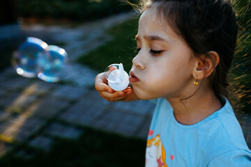 Portrait of cute girl blowing bubbles outdoors in the summer evenings 