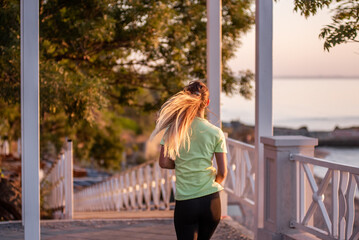 Obraz premium Young woman in sportswear is exercising, jogging on wooden stairs in the rays of the dawn sun.