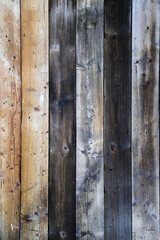 Old damaged wooden wall made of light-colored and dark-colored panels with multiple knots as a rural natural background