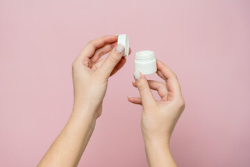 White jar or bottle with cream (ointment) in woman's hands. Facial care, bottle with cosmetic product