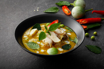 Exquisite Thai Cuisine: Green Curry Chicken, Infused with Aromatic Chili Paste and Creamy Sauce, Presented in a Black Bowl on a Textured Background