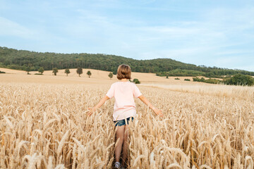 Naklejka na ściany i meble A happy school-age girl walks through a field of mature spikelets. Country life. summer holiday vacation. Vacation concept.