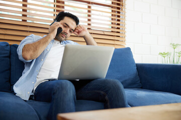 Fototapeta premium young handsome man using laptop computer and talking by smartphone at home