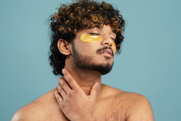  Portrait of young Indian man with patches under his eyes, naked torso after shower, touching his...