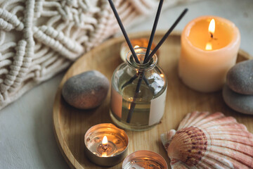 Relaxation, detention zone in the living or bedroom. Stones, sea shells as decor. Apartment natural aroma diffusor with ocean breeze fragrance. Burning candles on bamboo tray, cozy home atmosphere.