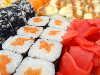 Assorted sushi set with baked soft cheese and flying fish caviar covered roll, maki sushi with salmon and pickled ginger in front. Japanese food background.   