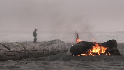 Beach fire in the foreground with a couple walking on chilly day on the Oregon Coast.