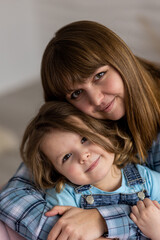 Portrait of mother with her daughter, cute little girl, at home on the sofa. Mother's or Women's day concept