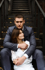 young wedding couple sits on a wooden staircase against the backdrop of an ecological house in the autumn season. newlyweds on the background of a wooden house in rustic style.