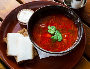Traditional Ukrainian borsch with sour cream in bowl, bread with bacon at plate
