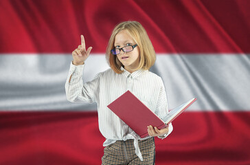 A girl with a book in her hand shows a gesture - attention on the background of the flag of Austria.