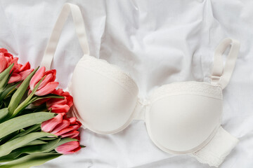 Gentle white lace bra on the bed with tulips. Women tender lingerie, underwear. Top view, close up. Flat lay, beauty blog or social media minimal concept. Present for Valentines, Women’s day